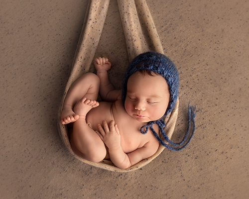 picture of newborn baby boy on a brown backdrop and blue bonnet in calgary