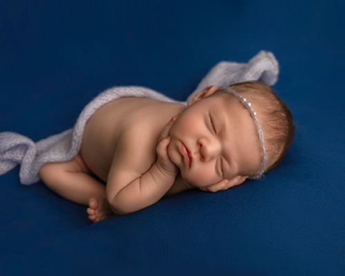 picture of newborn baby girl on blue backdrop with blue headband in calgary