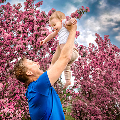 picture of a father lifting son up in front of cherry blossoms trees in calgary